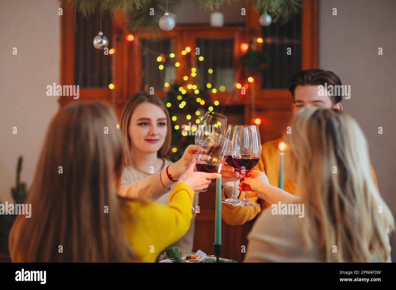 Happy young friends clinking glasses of wine over table decorated for Christmas celebration at home Stock Photo