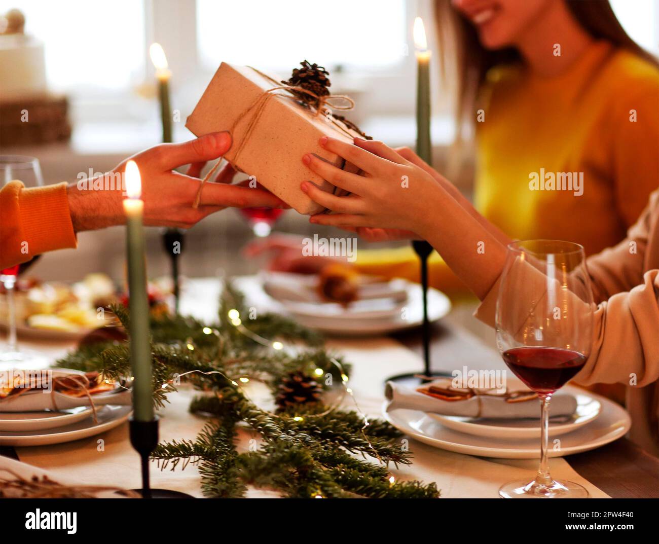 Happy person giving wrapped gift to friend while sitting at table and celebrating Christmas together Stock Photo