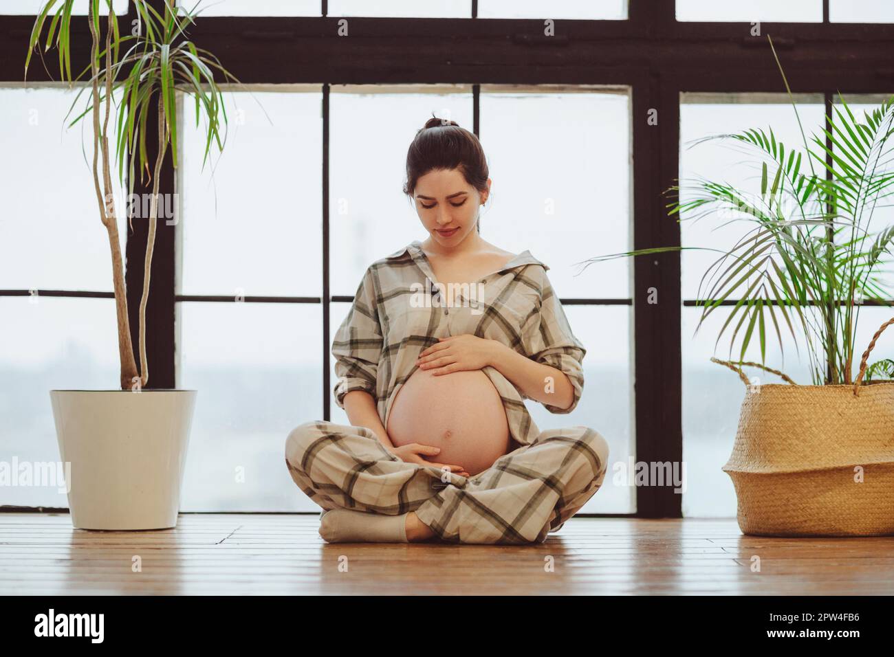 Full Length Of Young Calm Tranquil Pregnant Woman In Pajama Holding Belly While Sitting In Lotus 