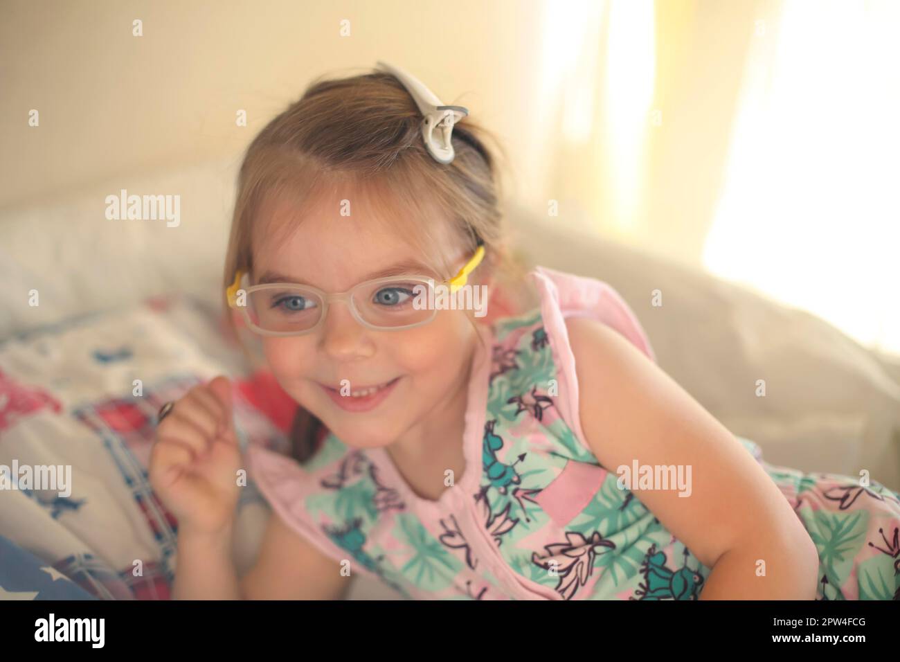 Childrens eyesight concept. Cute adorable little girl with deep blue eyes wearing eyeglasses smiling while playing at home. Happy positive kid with Stock Photo