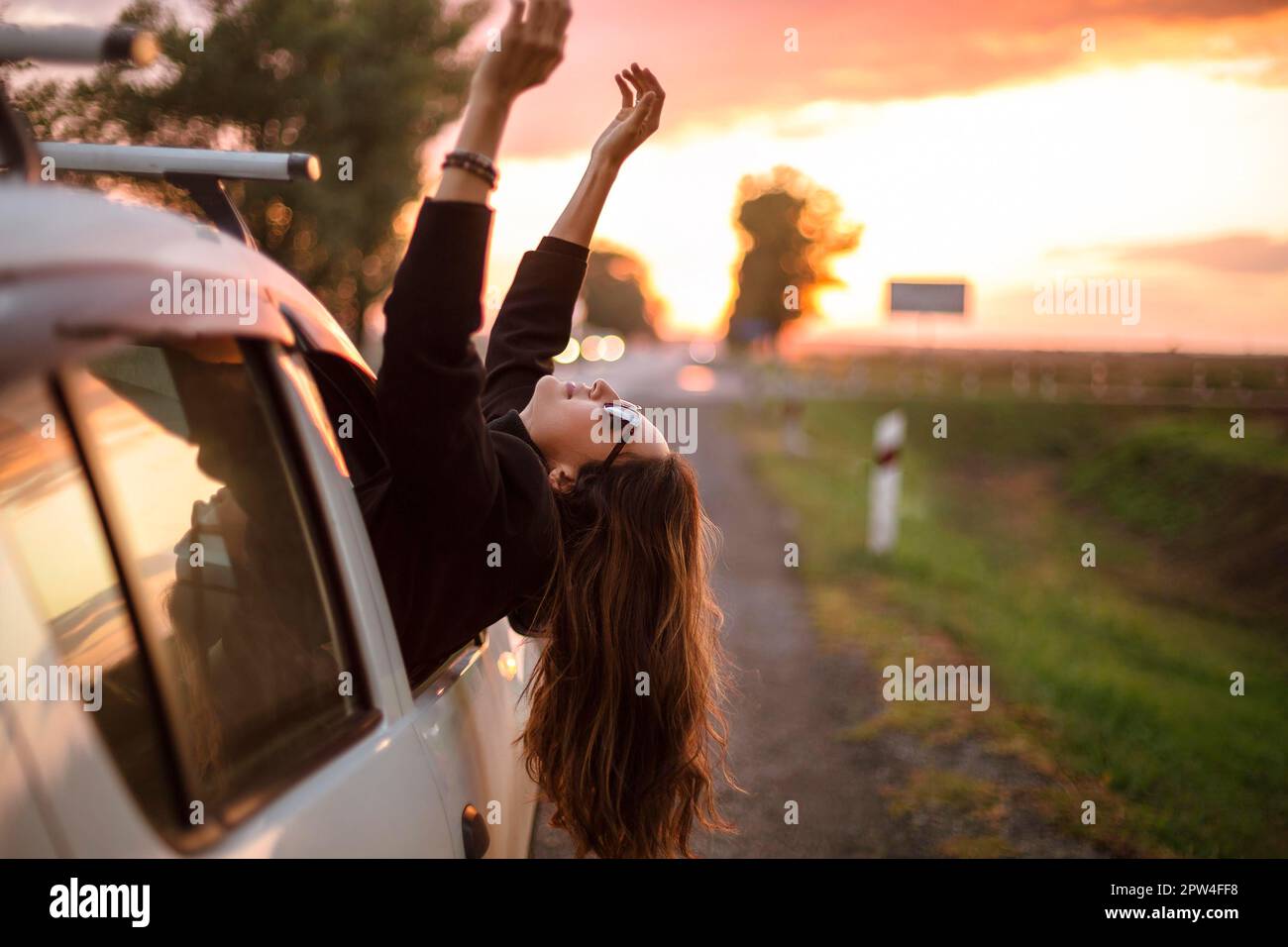 Young carefree woman traveler stretching out of car window while ...