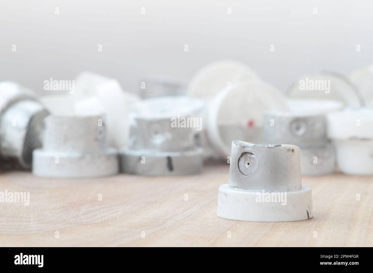 Several plastic nozzles from a paint sprayer that lie on a wooden surface against a gray wall background. The caps are smeared in chrome paint. The co Stock Photo