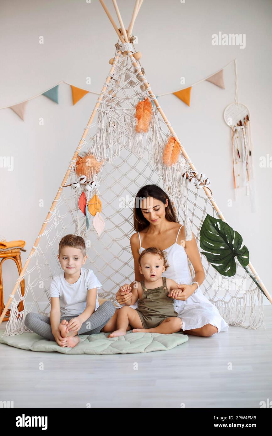 Young happy family loving mother with two kids sitting together in wigwam teepee at home, mom playing with preschool boy and toddler in play tent Stock Photo