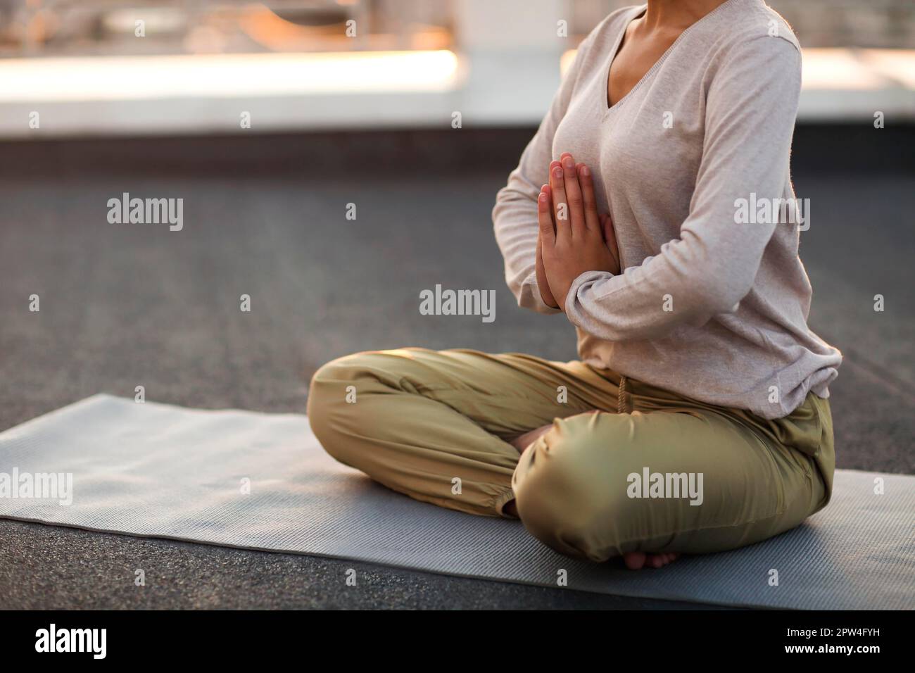 Cropped photo of unrecognizable woman sitting in lotus pose on mat and practicing yoga, female doing namaste gesture while meditating outdoors. Stock Photo