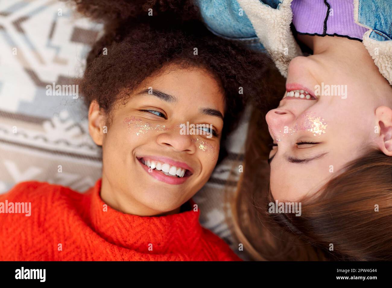 Female friendship. Two young diverse girlfriends of african american and caucasian ethnicity looking at each other with love while resting on plaid Stock Photo