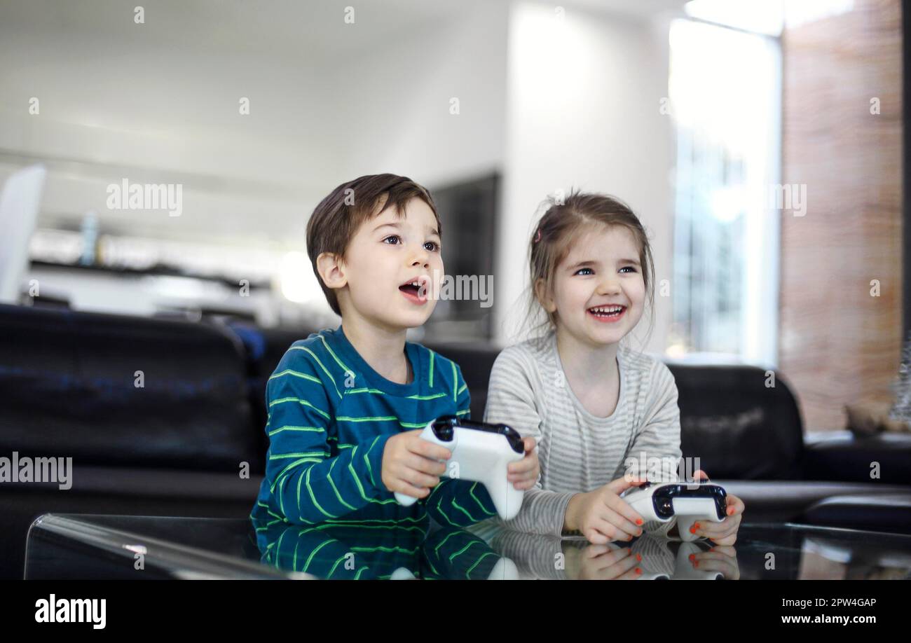 Joyful children with game controllers play video games at home. Kid's leisure Stock Photo