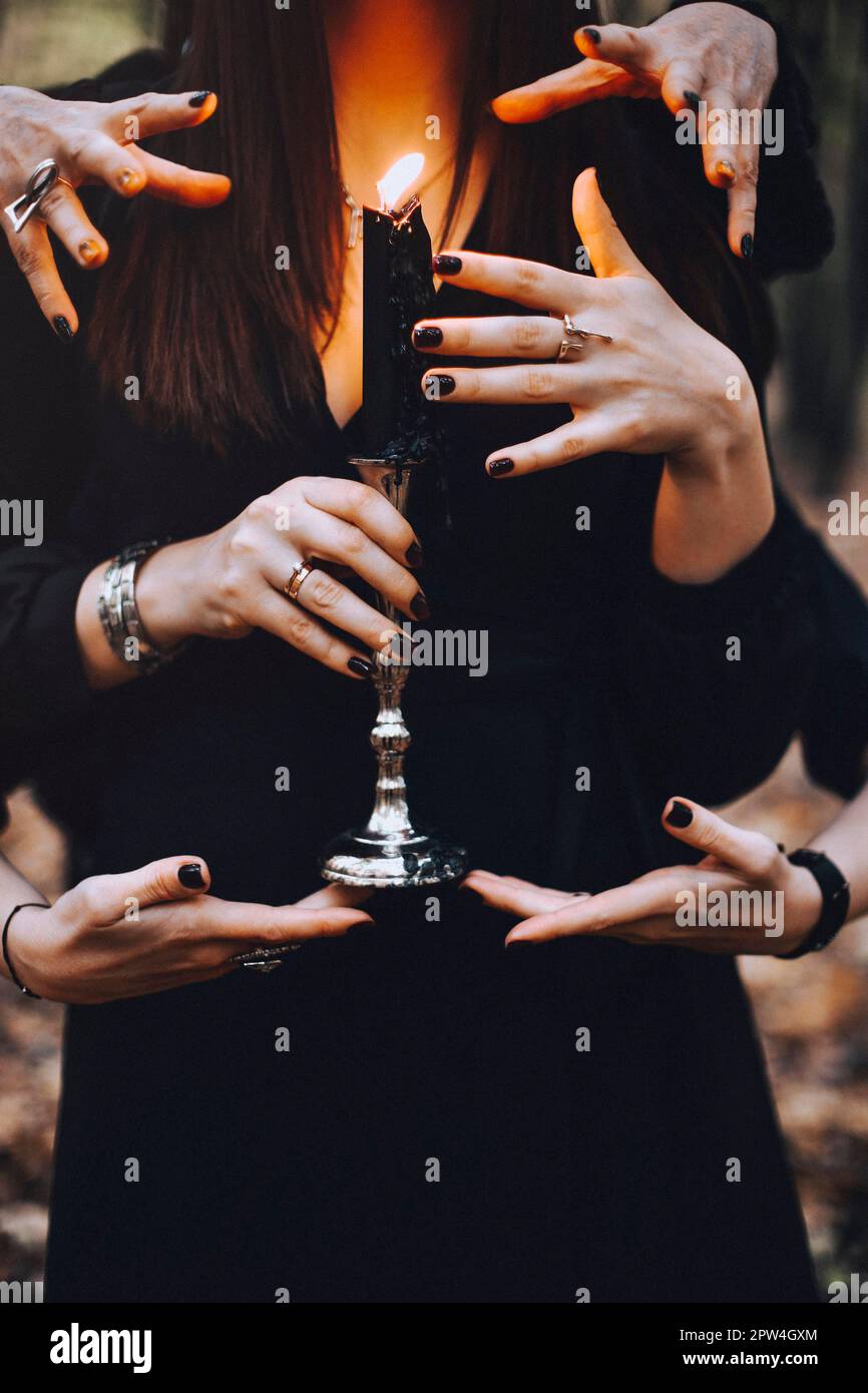 Mysterious photo of woman witch with burning candle being touched by many hands during magic ritual in dark autumn forest. Witchcraft concept Stock Photo