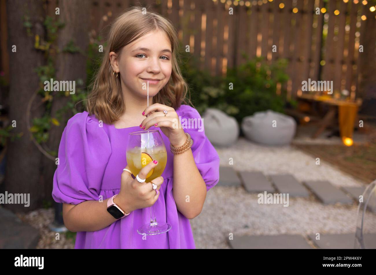Portrait of little girl drinking juice in a glass, decorated with fruits, with straw at outdoor park. Child in summer Stock Photo