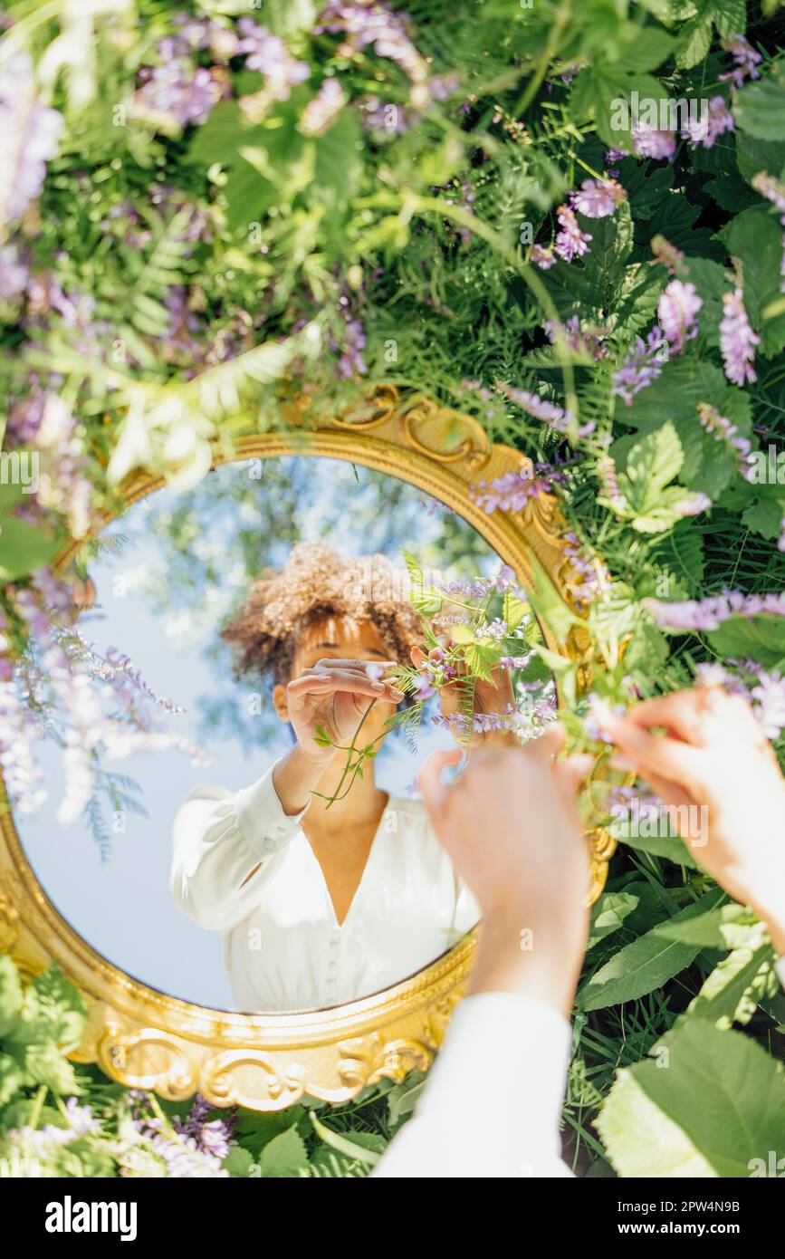Beautifal Mixed-race woman wearing white dress and sky reflection in round mirror on green spring grass. Nature concept Stock Photo
