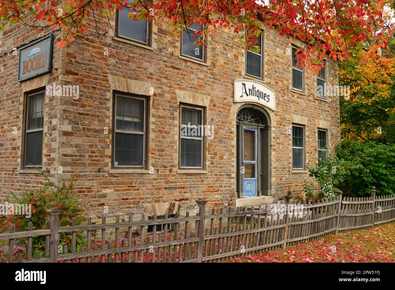 Fall foliage frames a beautiful stone building that houses an antique store and shop in New England on an autumn day Stock Photo