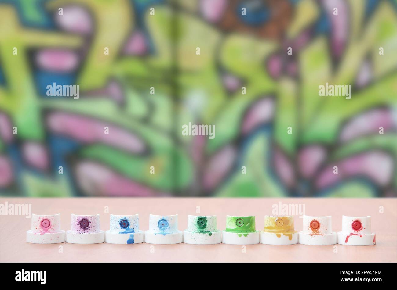 The soiled multicolored nozzles from the paint sprayer are lined up on a wooden table on a background of colored graffiti drawing in a wild style. The Stock Photo