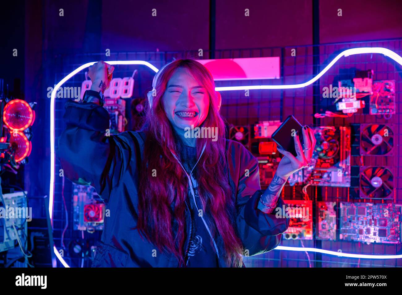 Happy asia girl gamer wear headphone competition play video game online  with smartphone colorful neon lights in living room at home. Esport  streaming game online, Home quarantine activity concept. Stock Photo