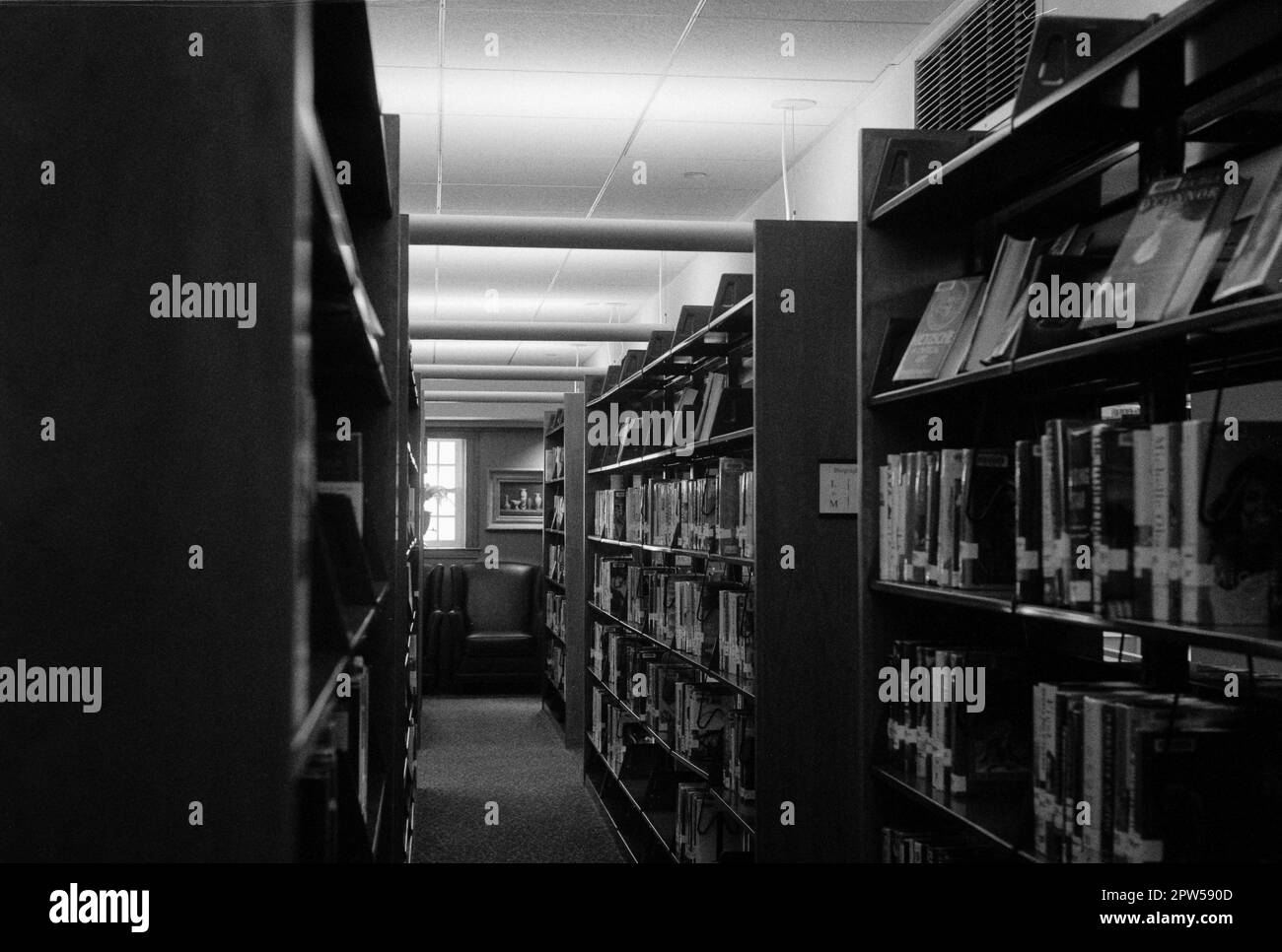 An isle with bookshelves on either side  in the Lucius Beebe Memorial Library. Wakefield, Massachusetts. The image was captured on analog black and wh Stock Photo