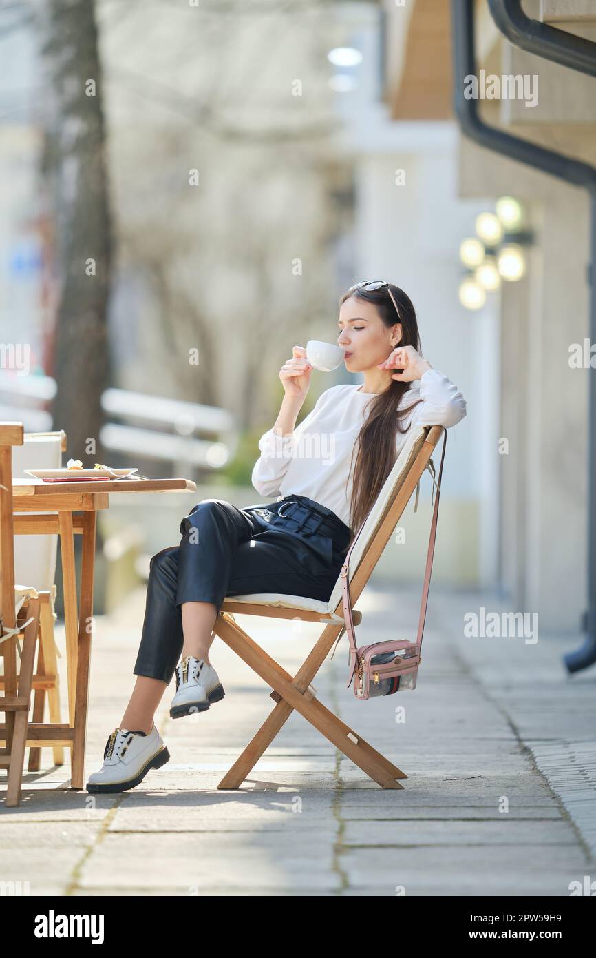 Pensive young woman sitting on the terrace of the cafe in sunny day and ...