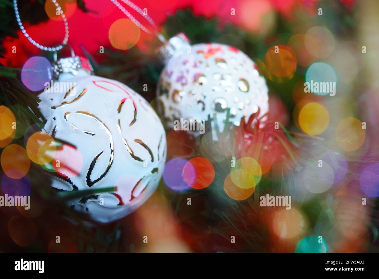 White trendy Christmas balls with sprinkles and a pattern on Christmas tree branches. Multicolored beautiful bokeh around the decorations. Postcard or Stock Photo