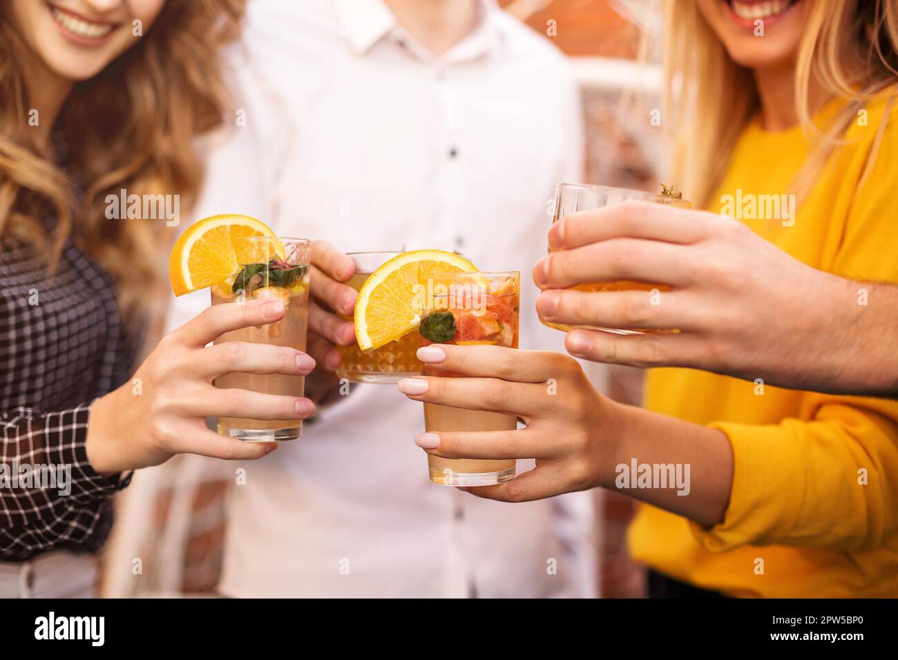 Anonymous men and women clinking glasses of fruit cocktails and proposing toast during party Stock Photo