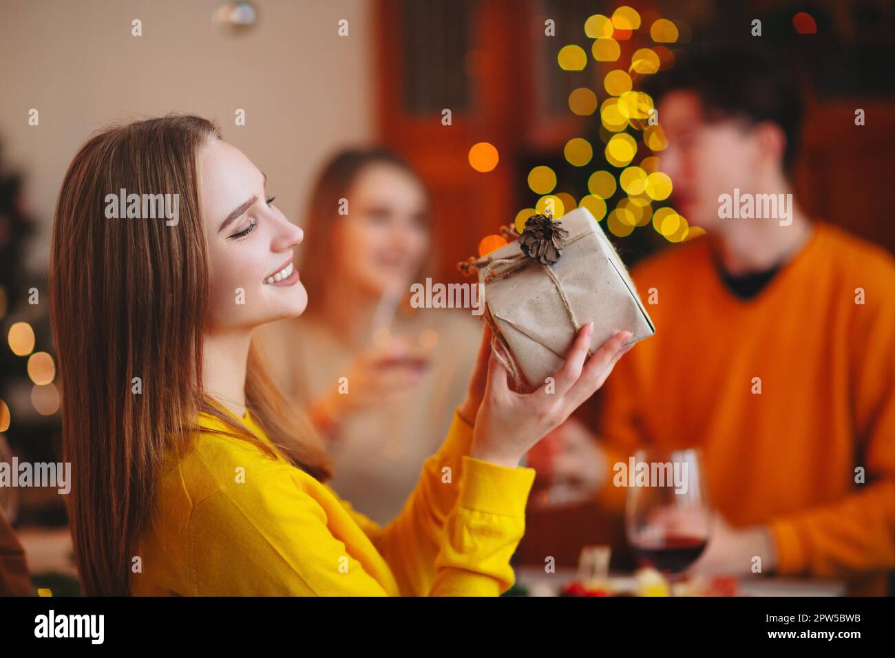 Young person giving wrapped gift to friend while sitting at table and celebrating Christmas together Stock Photo