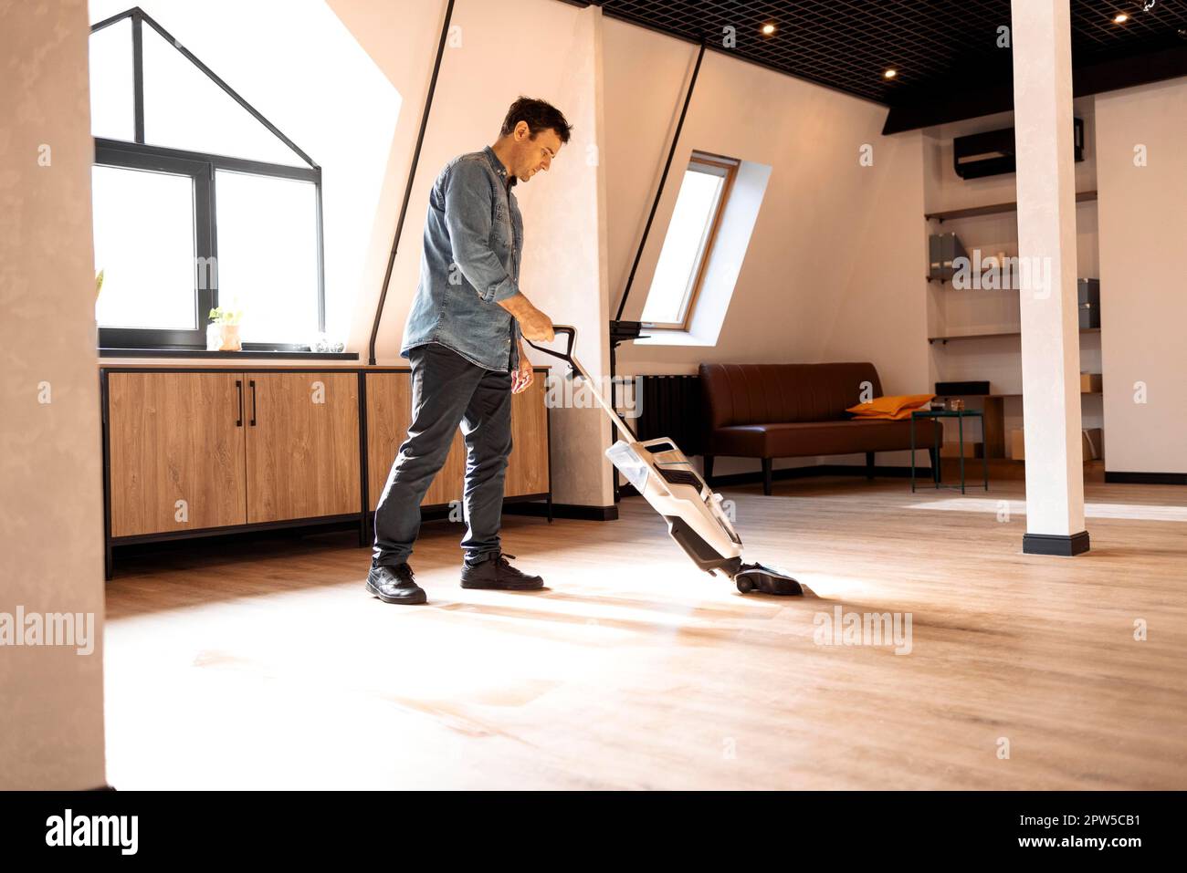 man vacuuming wooden floor in loft iving room with vacuum