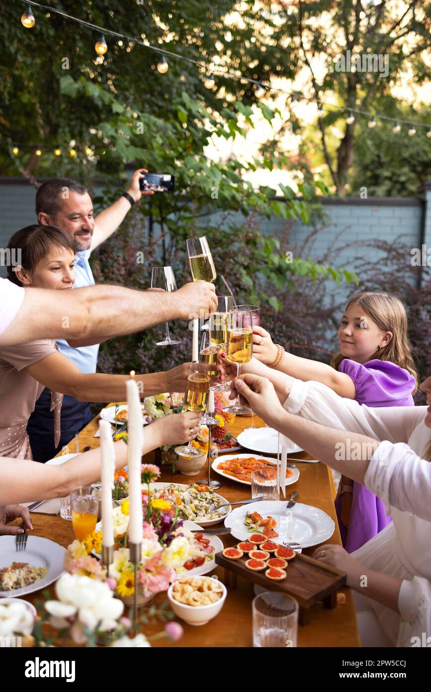 HAppy friends saying cheers and showing their champagne glasses full of sparkling wine to each other whilst enjoying an outdoor wedding party on a Stock Photo
