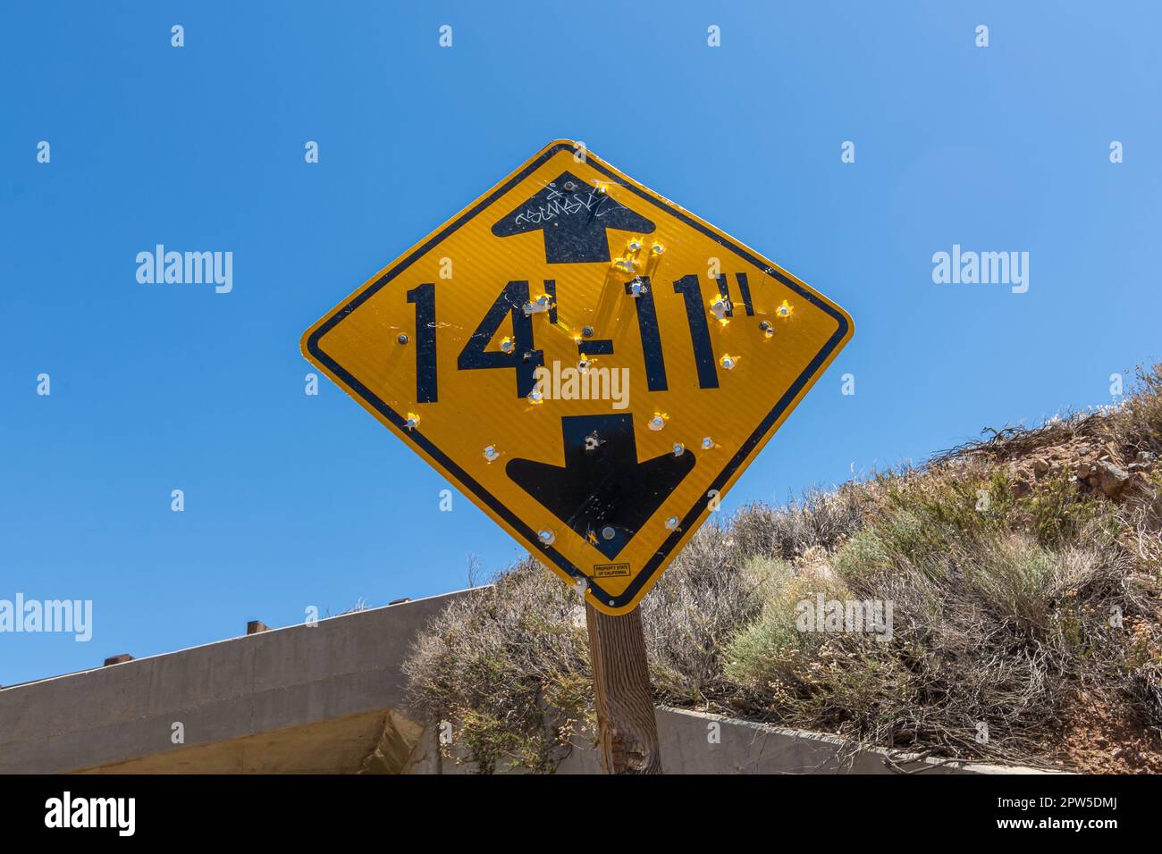 A sign with bullet holes in it warns of the maximum headroom ahead near Palmdale, California. Stock Photo