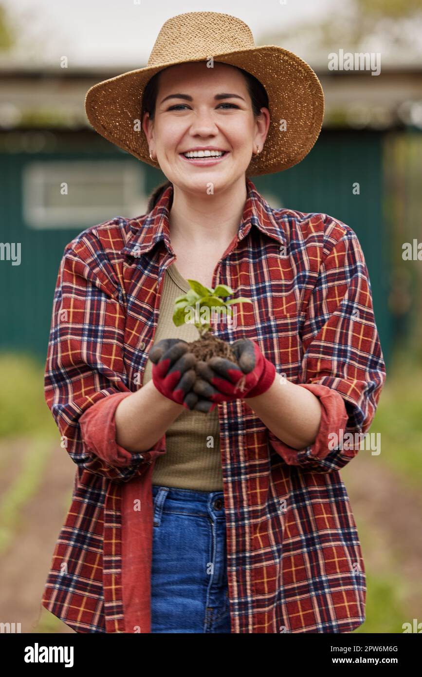 Sustainable farmer holding a plant or seedling outdoors smiling and happy about her organic farm or garden. Young female nature activist that is passi Stock Photo