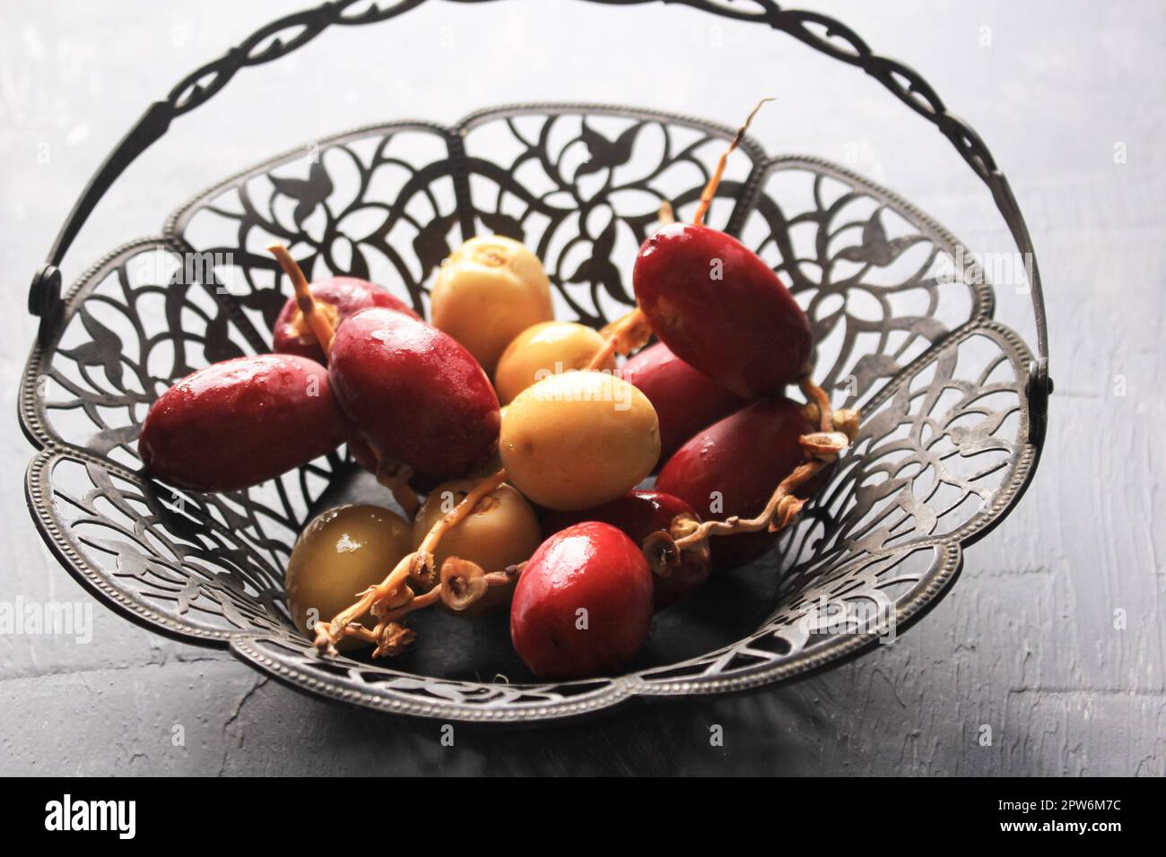 Red and Yellow Raw Dates Fruit or Kurma Muda (Ruthob) on Vintage Basket Above Rustic Background. Stock Photo