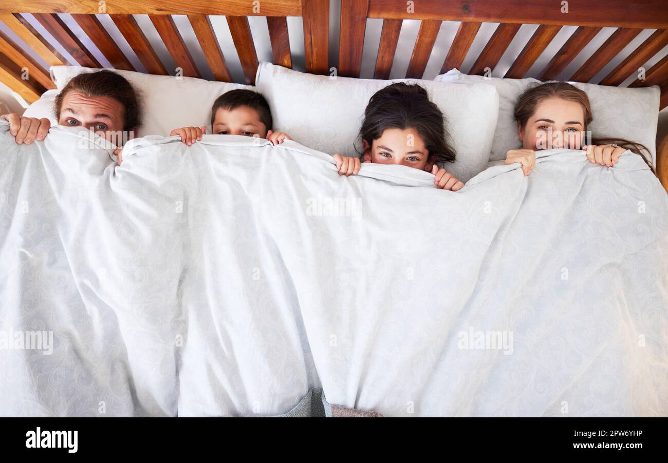 Above view of happy young caucasian family with two children lying in bed and pulling blanket
