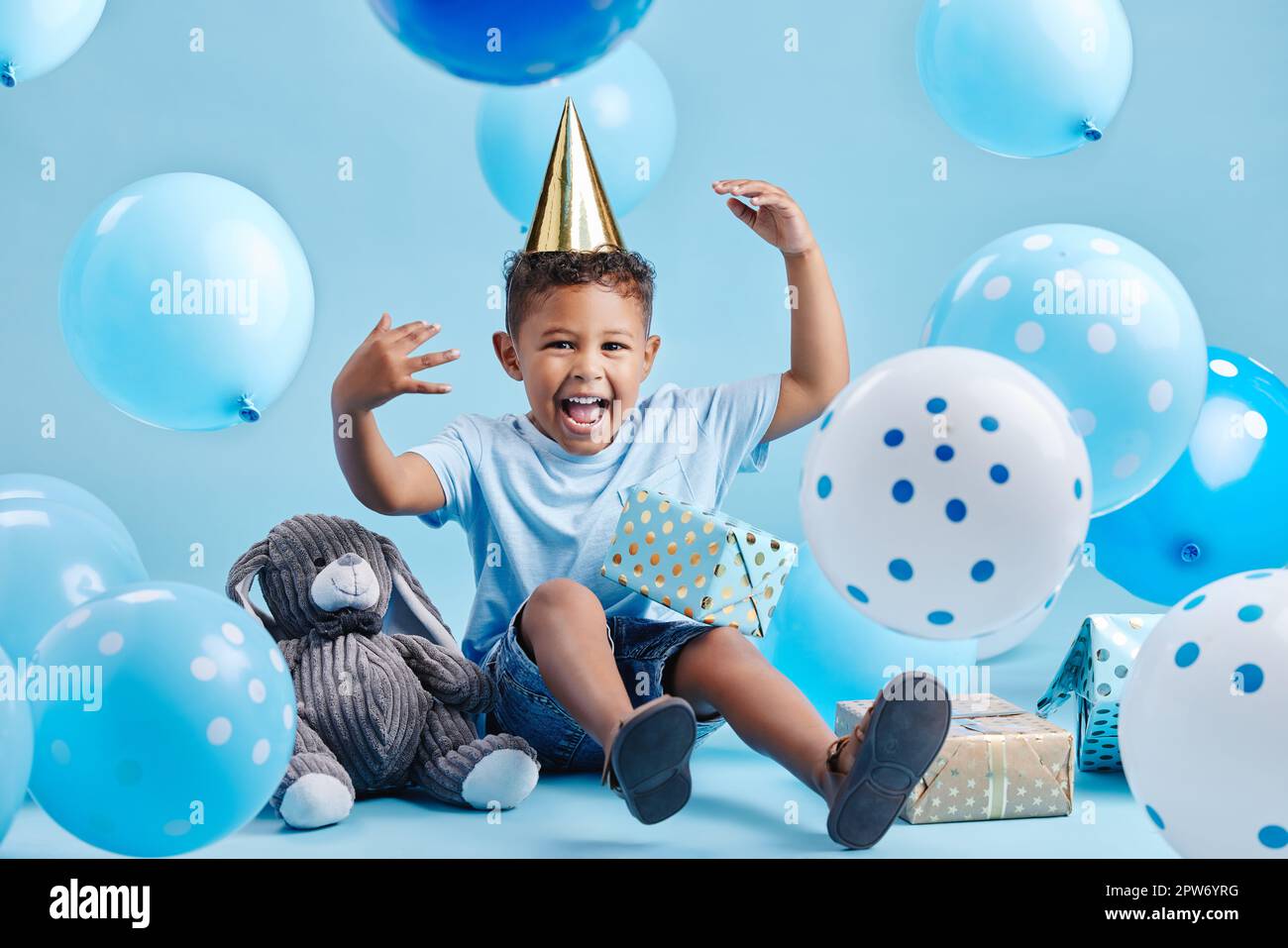 Excited little boy celebrating his birthday with balloons and gifts on