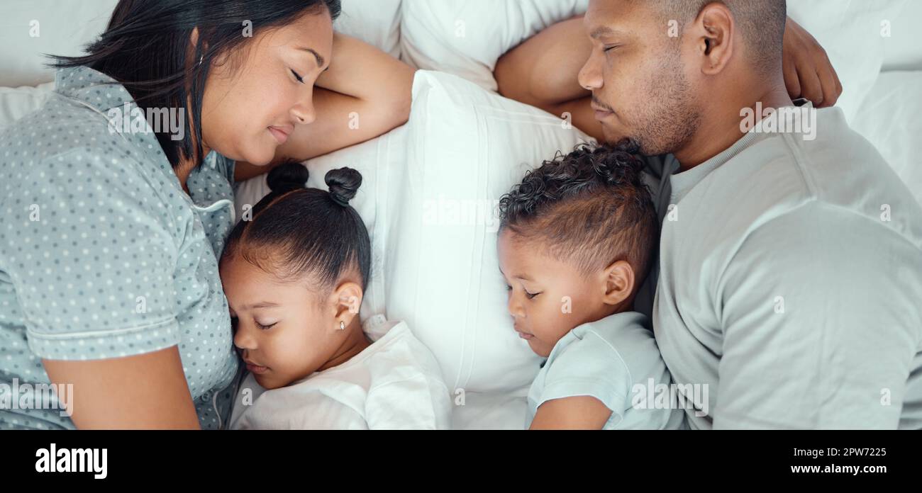 Happy family with two children sleeping together in their parents bed, from above. Loving