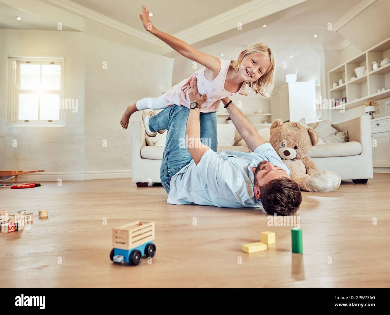 Father lifting his daughter. Dad lying on the floor lifting his child. Little girl flying in dads arms. Excited father playing with his kid. Father an Stock Photo