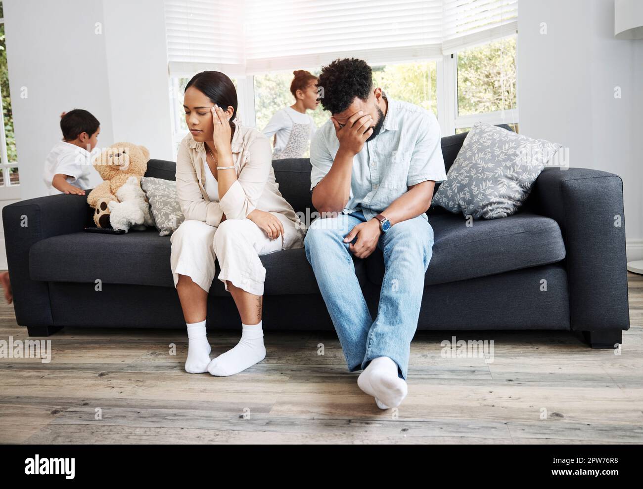 Sad, unhappy and stressed parents sitting on a couch near their children at home after an