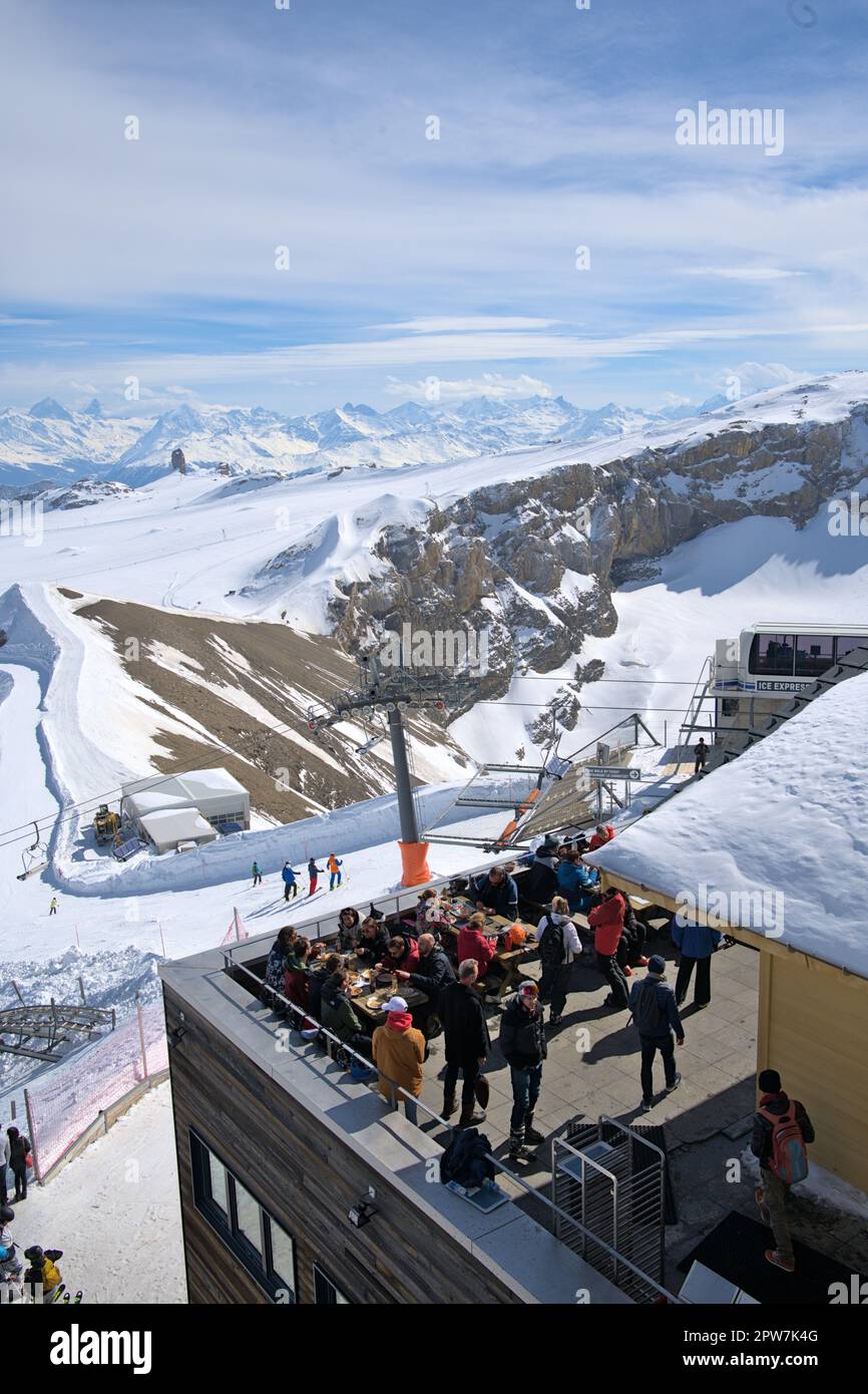Crowded picnic tables at a the restaurant at the peak of Glacier 3000 with skiers staring their descent. Skiing season at Ormont-Dessus, Switzerland Stock Photo