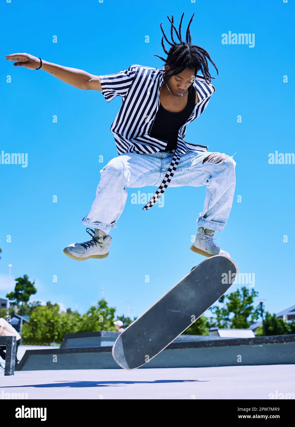 Cool young, stylish african american boy performing skate tricks on his board at the skate park. Focused young man performing ollies on his skateboard Stock Photo