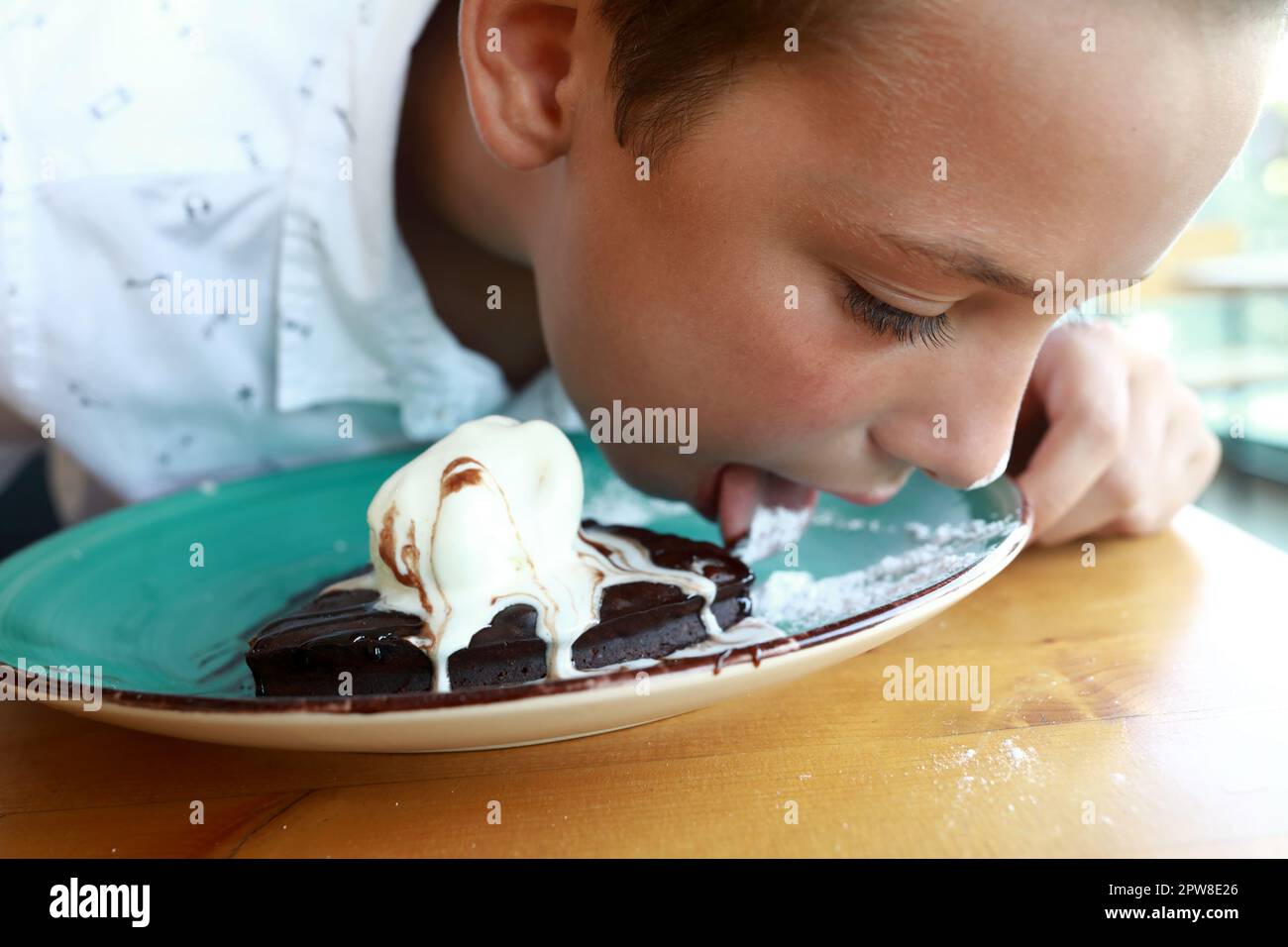 Child licks plate of brownie dessert in restaurant Stock Photo