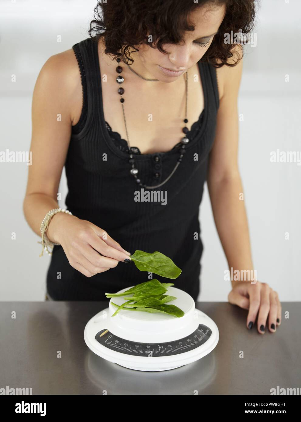 Woman, scale and spinach in kitchen for food, diet or eating disorder