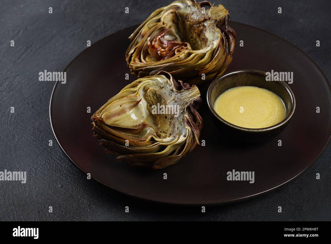 Oven roasted artichokes with garlic, rosemary and sauce on table Stock
