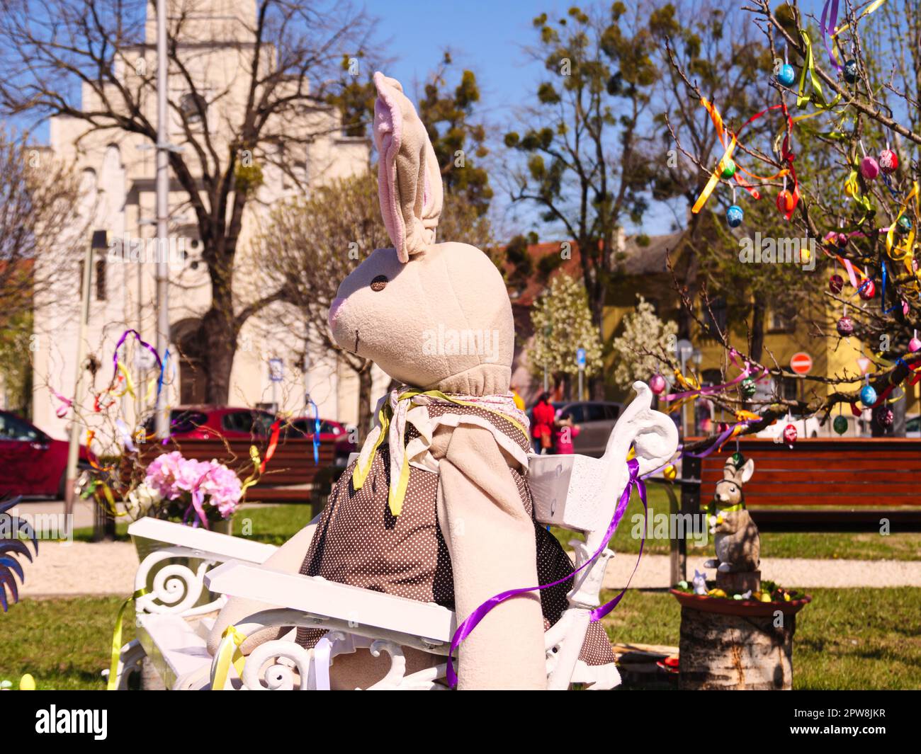 Happy Easter holiday in spring season with bunny decoration on a white bench . Colorful blurred background includes trees , green grass , people and... Stock Photo