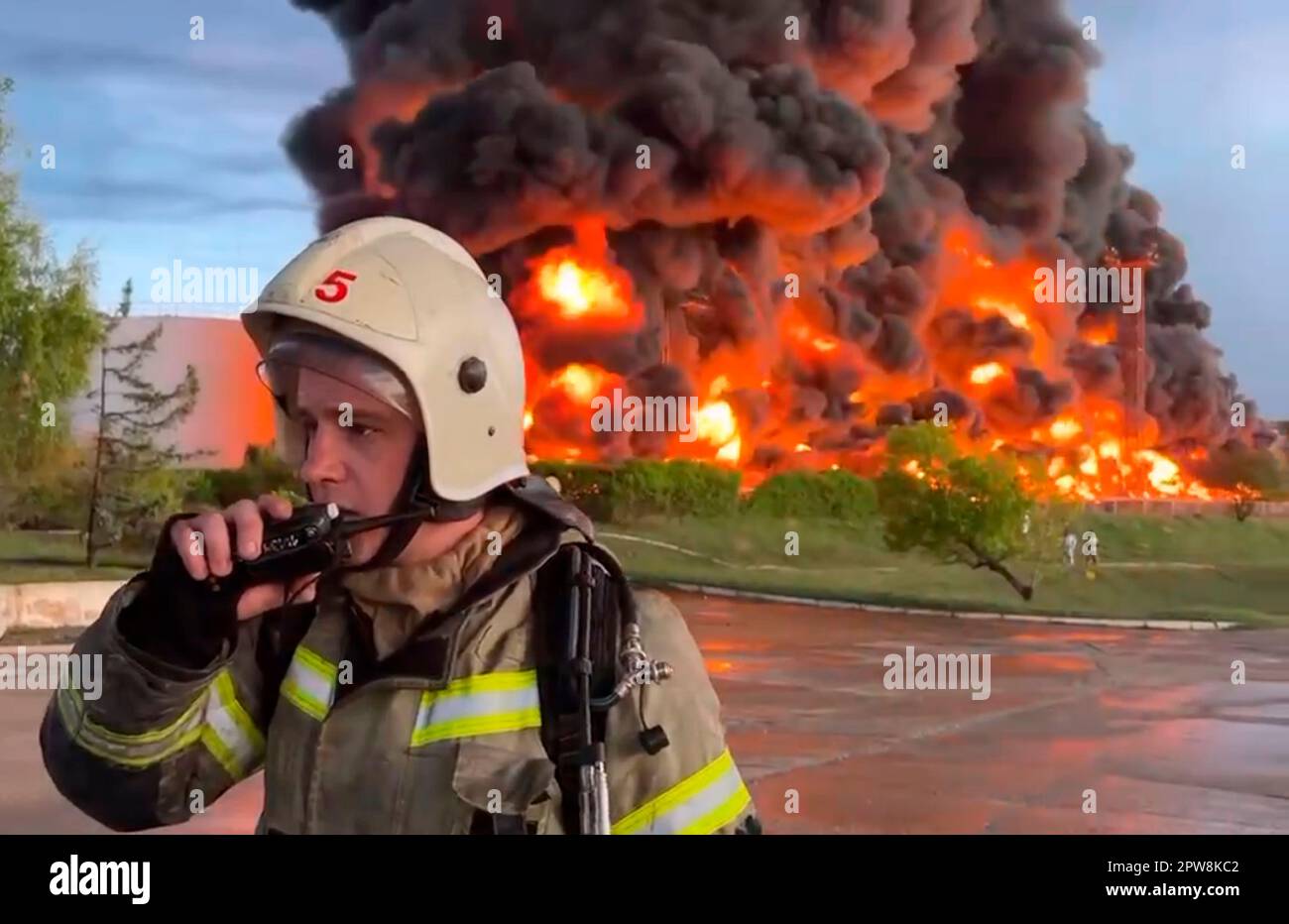 In this handout photo made from video released by the Governor of Sevastopol Mikhail Razvozhaev telegram channel on Saturday, April 29, 2023, a firefighter speaks on the walkie talkie as smoke and flame rise from a burning fuel tank in Sevastopol, Crimea. A massive fire erupted at an oil reservoir there after it was hit by a drone, a Russian-appointed official there reported on Saturday. (Sevastopol Governor Mikhail Razvozhaev telegram channel via AP) Stock Photo