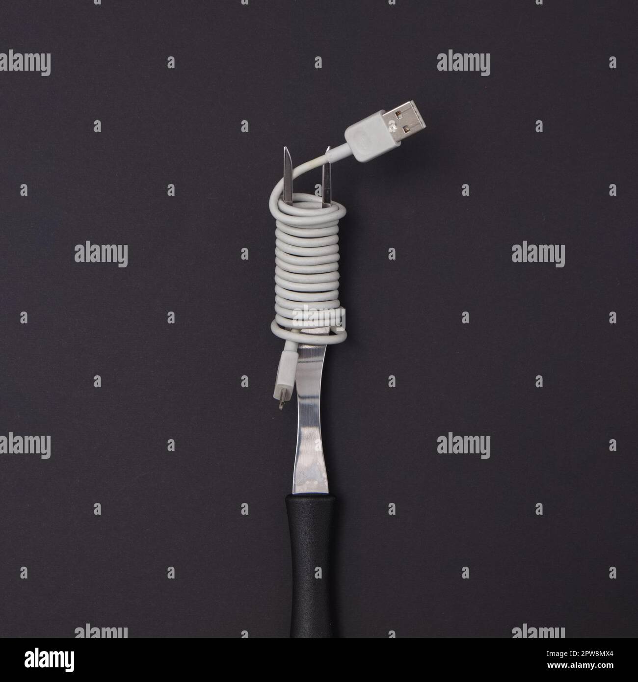 A fork with a USB cable wrapped like spaghetti on a black background. Minimal life style scene. Stock Photo
