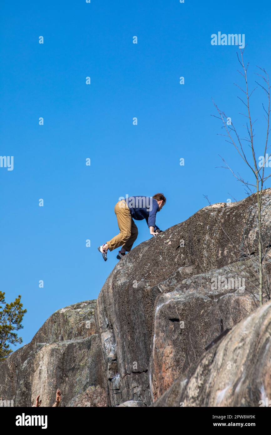 Boulderer or rock climber reaching the top of a cliff against clear blue sky at Humallahdenkalliot in Meilahti district of Helsinki, Finland Stock Photo