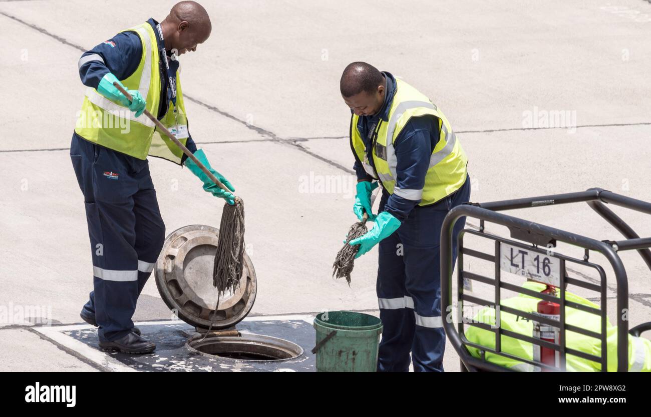 two African black men airport workers or employees in overalls and high vis vests clean a fuel tank at Lanseria airport, Gauteng, South Africa Stock Photo