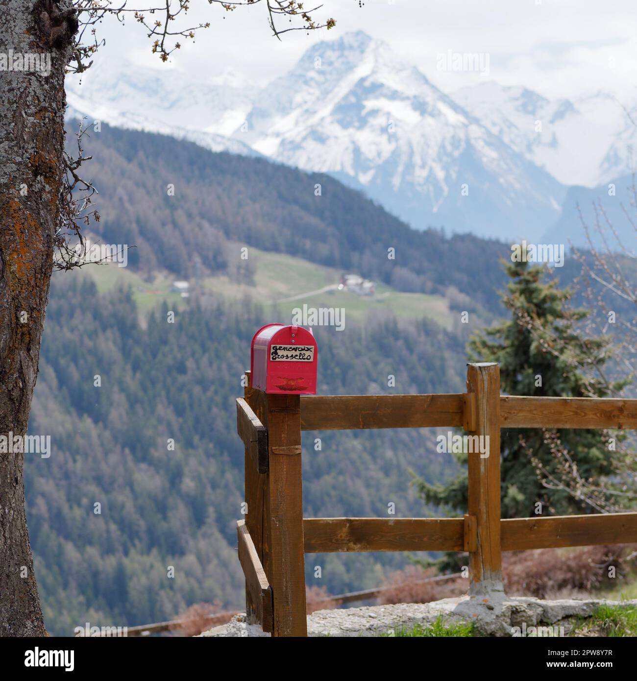 Red post box on a wooden fence in the alpine town of Lignan in the Aosta Vally, NW Italy Stock Photo