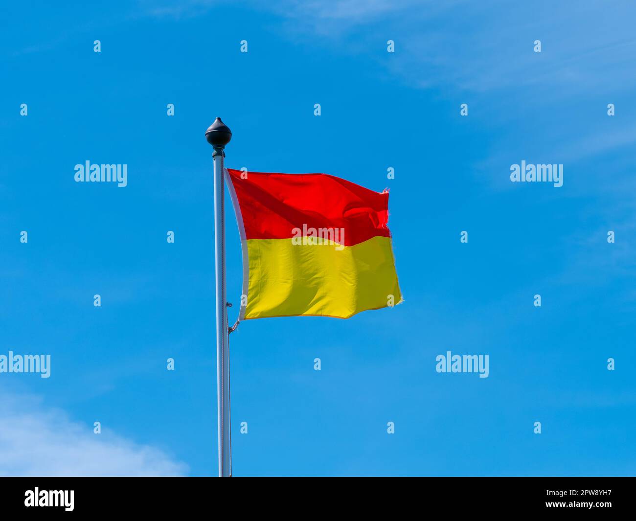 A red and yellow flag allowing swimming on the beach. flag on a blue