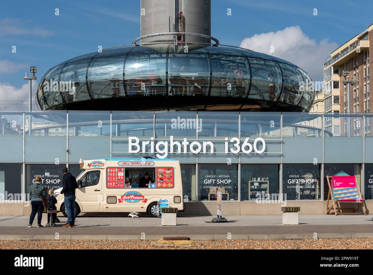 Brighton i360 observation tower starting to rise with the company logo in front of it, watched by a family enjoying a day out.  April 2023 Stock Photo