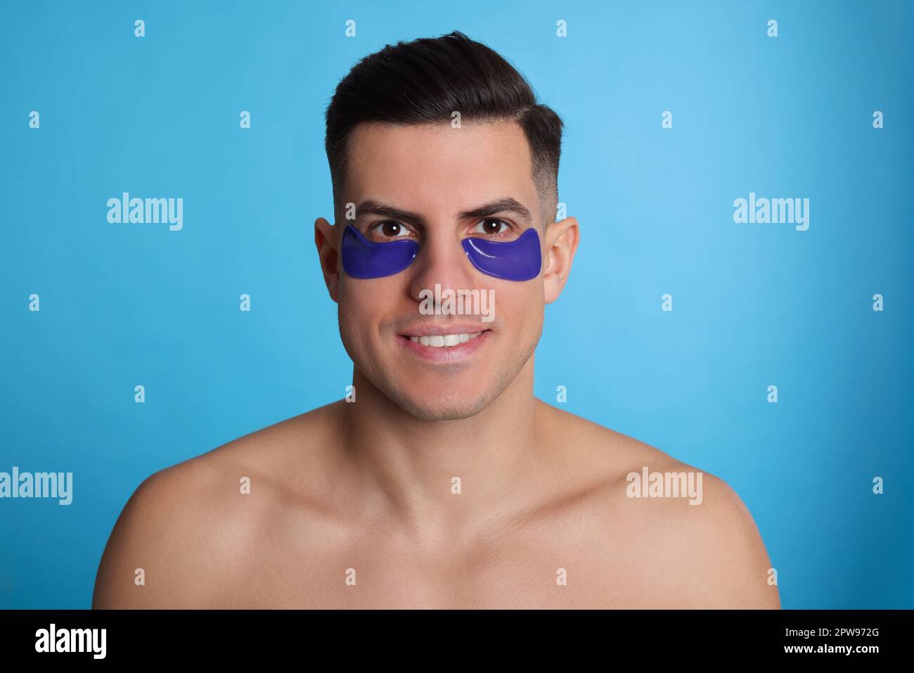 Man with under eye patches on light blue background Stock Photo - Alamy