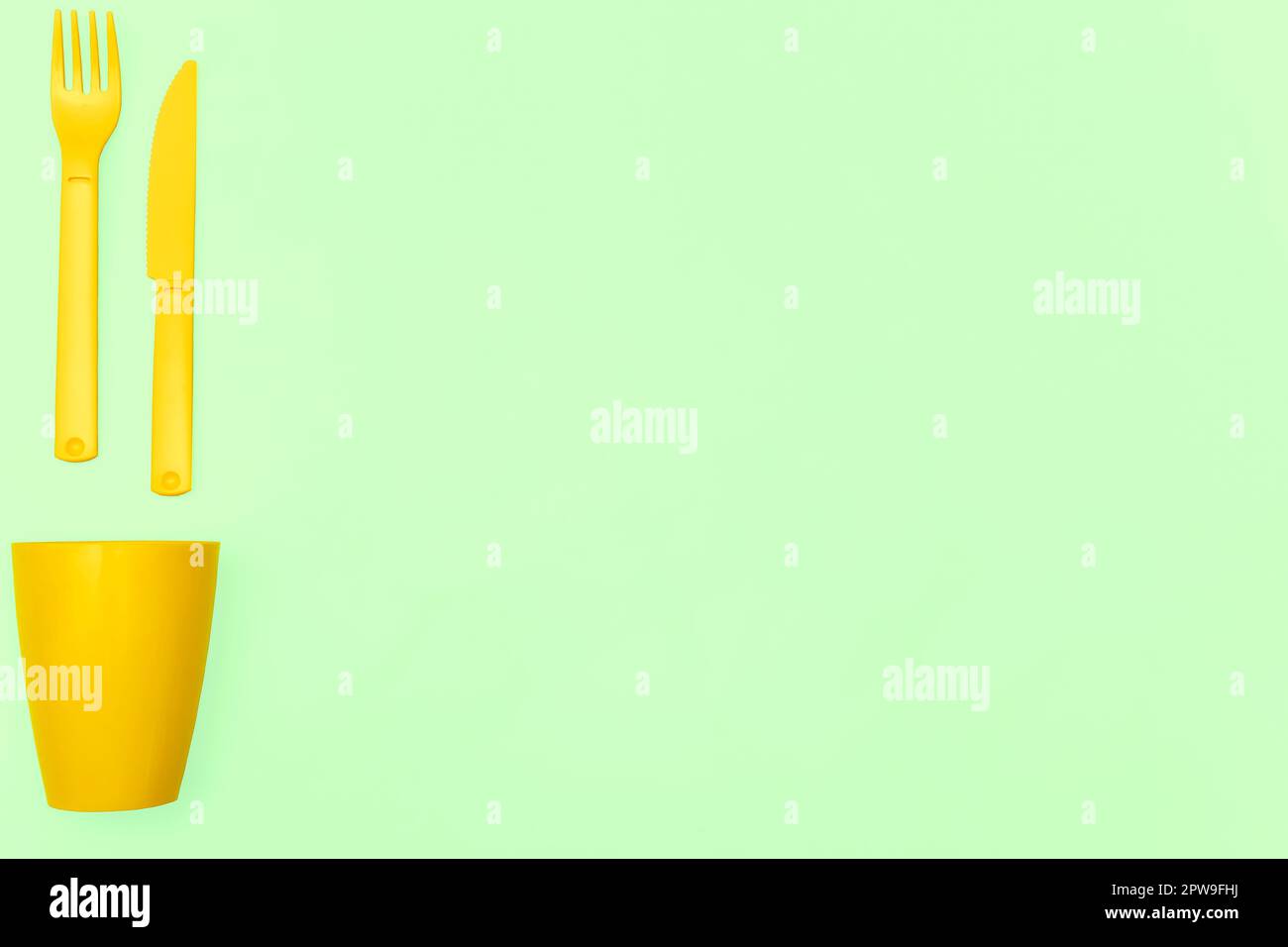 Plastic spoons, forks and a glass for camping, isolated on lime green