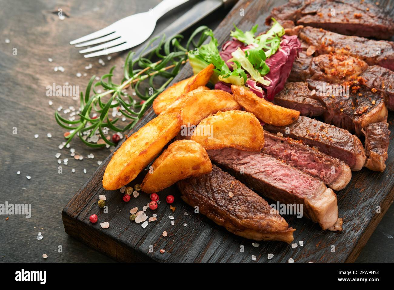 Steaks. Sliced grilled meat steak New York, Ribeye or Chuck roll with with garnished with salad and french fries on black marble board on old wooden b Stock Photo