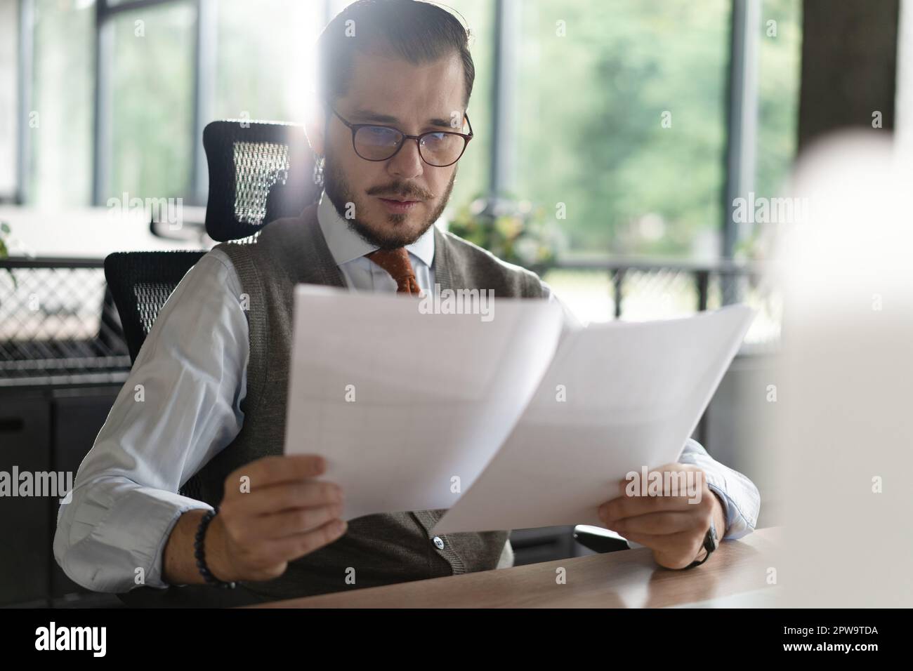 Satisfied man reading paper documents, letters, receiving pleasant news, working at workplace, sitting on desk, successful businessman, freelancer loo Stock Photo