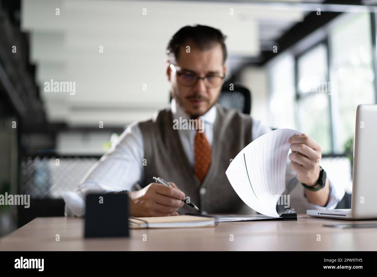Satisfied man reading paper documents, letters, receiving pleasant news, working at workplace, sitting on desk, successful businessman, freelancer loo Stock Photo
