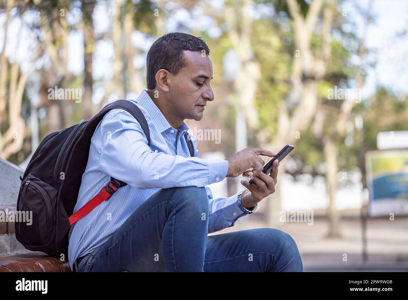 Young latino man sitting on some stairs looking at his mobile phone. Stock Photo